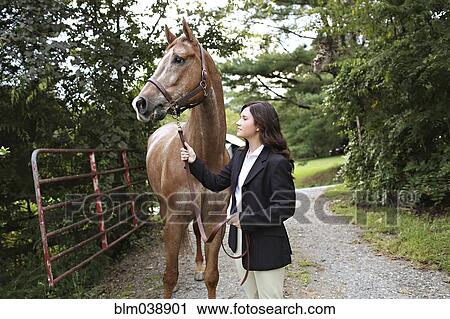 Stock Image - Equestrian woman walking horse on dirt path. Fotosearch