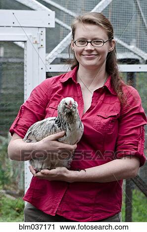 Stock Image - Farmer holding chicken in yard. Fotosearch