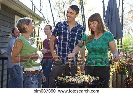 Stock Image - Friends grilling vegetables in backyard. Fotosearch