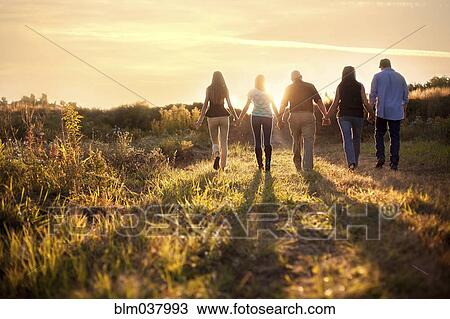Stock Image - Friends holding hands in sunny rural field. Fotosearch