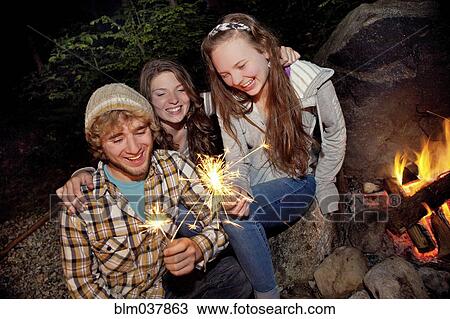 Stock Image - Friends playing with sparklers near campfire. Fotosearch