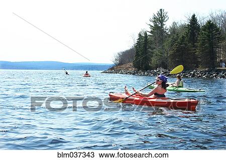 Stock Image - Friends rowing kayaks in lake. Fotosearch