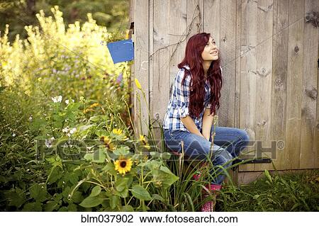 Stock Image - Gardener sitting near wooden shed in backyard. Fotosearch
