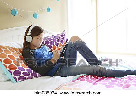 Girl listening to headphones with digital tablet on bed View Large Photo Image Picture - Girl listening to headphones with digital tablet on bed. Fotosearch