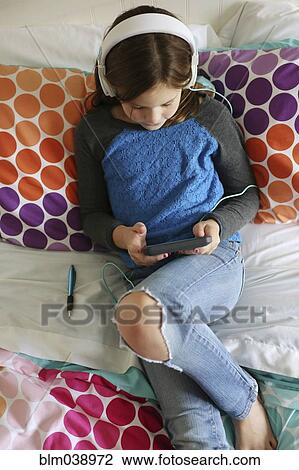 Stock Image - Girl listening to headphones with digital tablet on bed. Fotosearch