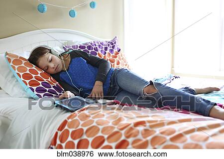 Girl listening to headphones with digital tablet on bed View Large Photo Image Stock Photograph - Girl listening to headphones with digital tablet on bed. Fotosearch