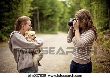 Girl photographing friend holding puppy in forest View Large Photo Image Stock Photo - Girl photographing friend holding puppy in forest. Fotosearch