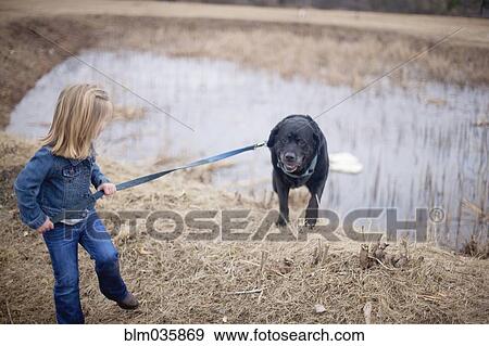 Stock Photo - Girl pulling dog on leash near rural pond. Fotosearch