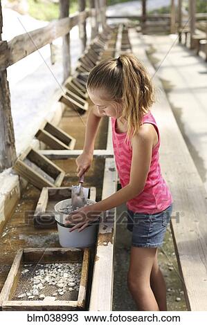 Stock Image - Girl shoveling rocks in bucket in trough. Fotosearch