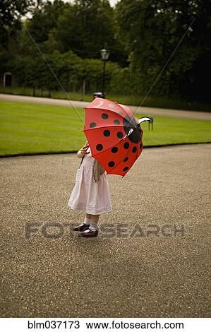 Stock Image - Girl standing under umbrella in park. Fotosearch