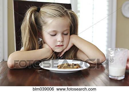 Girl staring at cookie with milk at table View Large Photo Image Stock Photograph - Girl staring at cookie with milk at table. Fotosearch