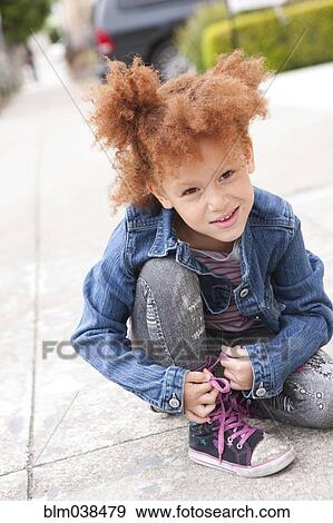 Stock Photo - Girl tying sneaker shoelaces on sidewalk. Fotosearch