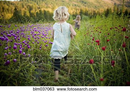 Stock Image - Girl walking in rural field of flowers. Fotosearch