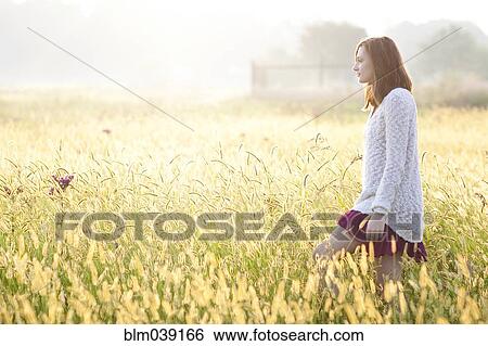 Stock Photograph - Girl walking in tall grass in rural field. Fotosearch