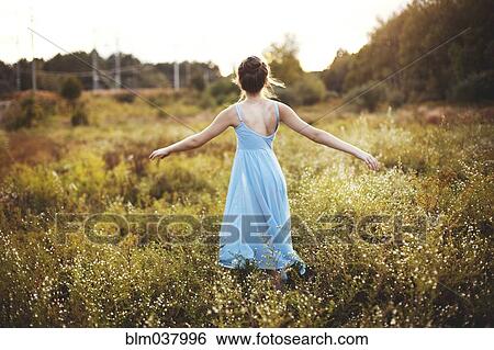 Stock Photograph - Girl walking with arms outstretched in rural field. Fotosearch