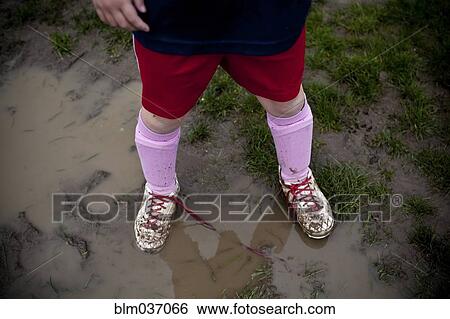 Stock Photograph - Girl wearing sneakers in mud puddle. Fotosearch