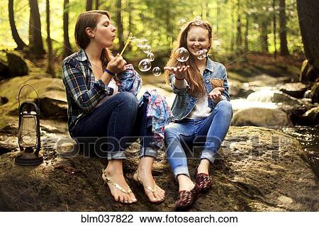 Stock Image - Girls blowing bubbles on forest rock. Fotosearch