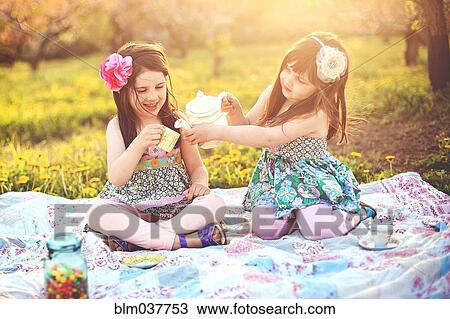 Stock Image - Girls having tea party picnic in rural field. Fotosearch
