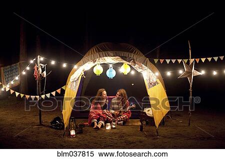 Stock Photography - Girls relaxing in camping tent at night. Fotosearch