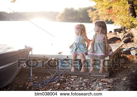 Picture - Girls sitting on wooden dock on rural lake. Fotosearch