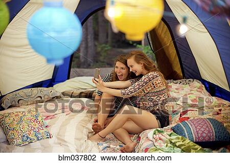 Stock Image - Girls taking selfie with cell phone in camping tent. Fotosearch