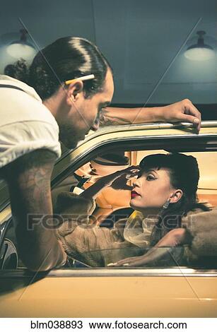 Stock Image - Glamorous couple talking in vintage car. Fotosearch