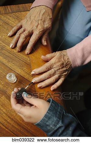 Stock Image - Granddaughter applying painting fingernails of grandmother. Fotosearch