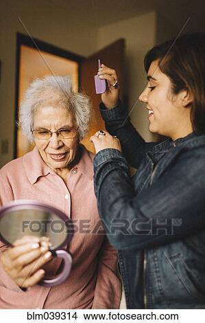 Picture - Granddaughter combing hair of grandmother holding mirror. Fotosearch
