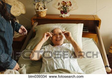 Granddaughter giving grandmother eyeglasses in bed View Large Photo Image Picture - Granddaughter giving grandmother eyeglasses in bed. Fotosearch