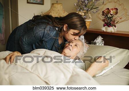 Stock Photography - Granddaughter kissing forehead of grandmother in bed. Fotosearch