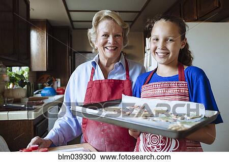 Stock Image - Grandmother and granddaughter baking cookies in kitchen. Fotosearch