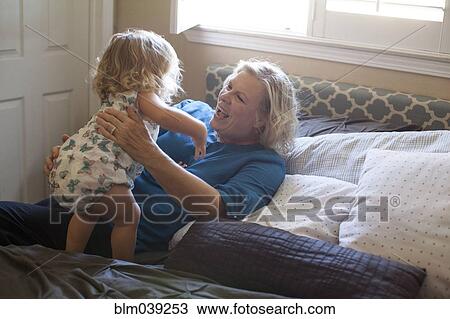 Stock Image - Grandmother and granddaughter playing on bed. Fotosearch