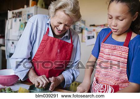 Stock Image - Grandmother and granddaughter squeezing juice in kitchen. Fotosearch