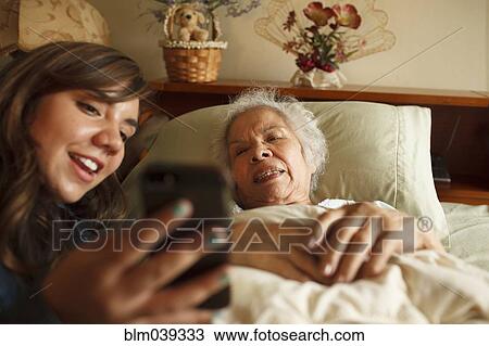 Stock Image - Grandmother and granddaughter taking selfie with cell phone in bed. Fotosearch
