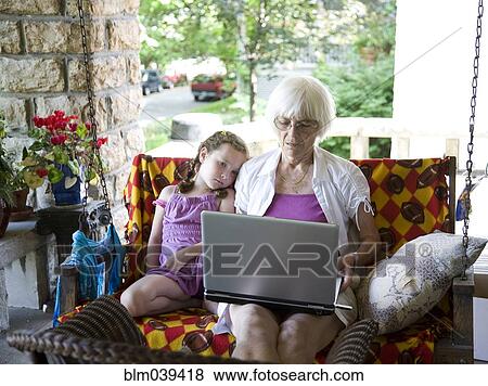 Stock Photo - Grandmother and granddaughter using laptop on porch. Fotosearch