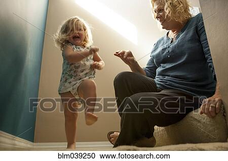 Stock Image - Grandmother watching granddaughter walking on staircase. Fotosearch