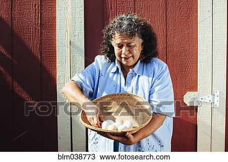 Stock Image - Hispanic farmer counting fresh eggs in basket. Fotosearch