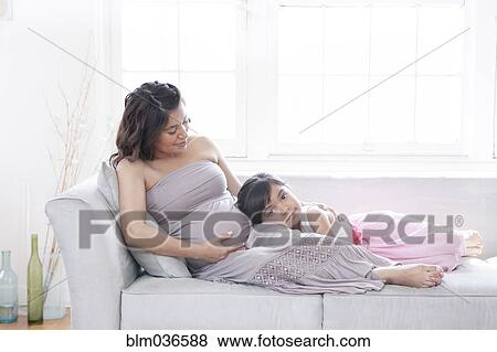 Stock Photo - Hispanic girl listening to belly of pregnant mother on sofa. Fotosearch