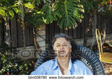 Stock Image - Hispanic woman relaxing in backyard. Fotosearch