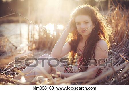 Stock Image - Hispanic woman sitting in tall grass in field. Fotosearch