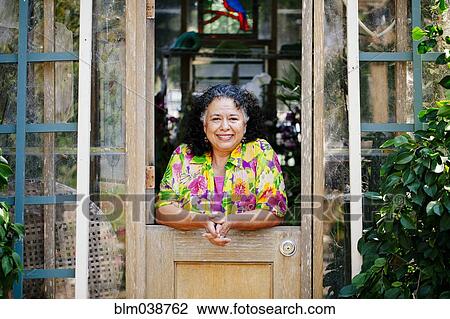 Stock Image - Hispanic woman smiling in garden greenhouse doorway. Fotosearch