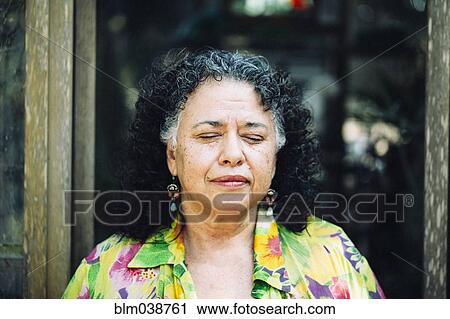 Stock Image - Hispanic woman standing with eyes closed outdoors. Fotosearch