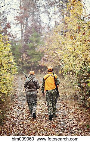 Stock Image - Hunters in camouflage carrying rifles in forest. Fotosearch