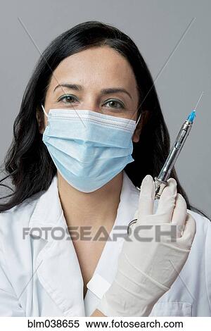 Stock Photography - Indian dentist in surgical mask holding syringe. Fotosearch