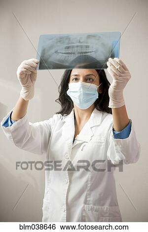 Stock Photograph - Indian dentist in surgical mask examining x-rays. Fotosearch