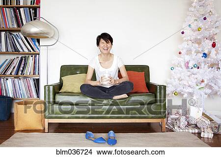 Picture - Japanese woman drinking coffee near Christmas tree. Fotosearch