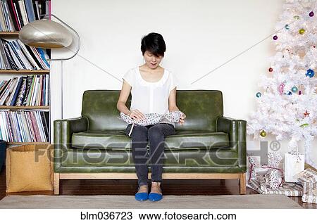 Stock Image - Japanese woman opening gift near Christmas tree. Fotosearch