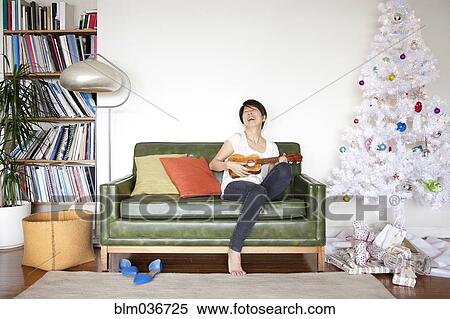 Stock Photography - Japanese woman playing ukulele near Christmas tree. Fotosearch