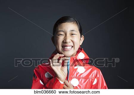 Stock Image - Laughing Asian girl zipping up raincoat. Fotosearch