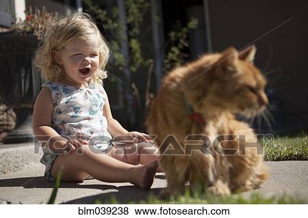 Stock Photo - Laughing girl admiring cat in backyard. Fotosearch